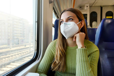 Female commuter wearing medical protective mask looking through the window sitting on train