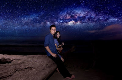 Woman sitting on rock by sea against sky at night