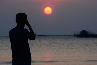 Silhouette man standing on beach against sky during sunset