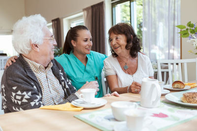 Young caregiver with senior couple during breakfast at nursing home