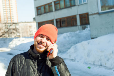 Portrait of man in warm clothing talking on mobile phone against building