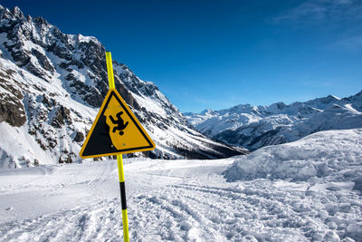 Road sign by snow covered mountains against sky