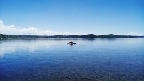 Mid distance view of friends sitting in boat on lake against blue sky