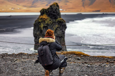 Rear view of woman sitting on rock at beach