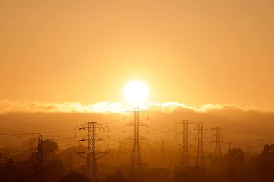 Silhouette electricity pylons against orange sky