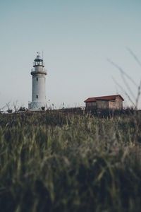 Lighthouse on field by building against sky