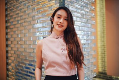 Portrait of a smiling young woman standing against wall