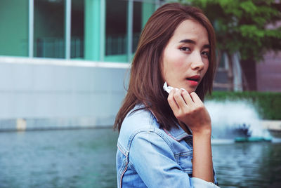 Portrait of beautiful young woman wiping sweat with tissue paper against fountain