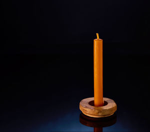Not burning candle staying at the black glass in the wooden candleholder. black back, blue light. 