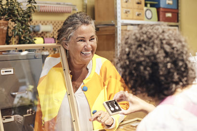 Happy saleswoman assisting female customer buying earring at store