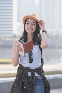 Portrait of smiling woman holding smart phone while standing outdoors