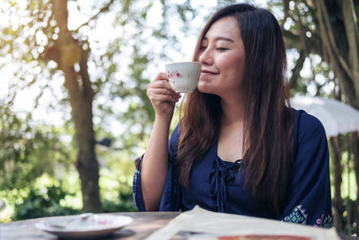 Woman drinking coffee in cup against trees