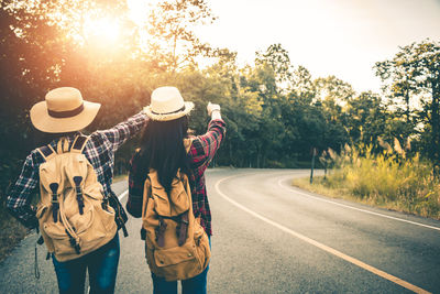 Rear view of people standing on road by trees