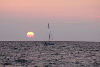 Sailboat sailing in sea at sunset