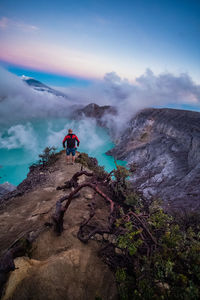 Rear view of man on rock by mountain against sky