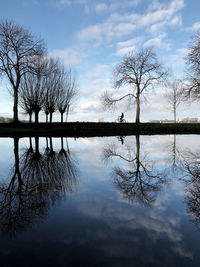 Reflection of bare trees in lake against sky