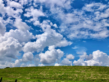 A vivid pattern of little white clouds in a blue sky over a green dike