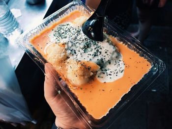 High angle view of hand holding curry in plastic plate