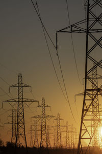 Low angle view of electricity pylon against sky during sunset