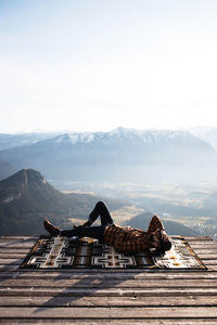 Unrecognizable male tourist lying on blanket at viewpoint and enjoying scenery of mountain ridge in morning