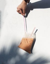 Cropped image of hand holding teh tarik against white wall