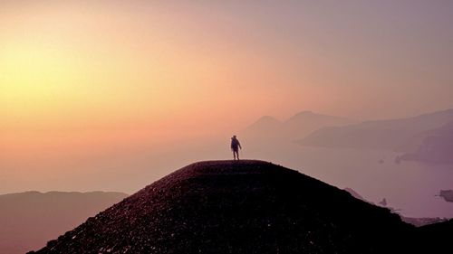 Silhouette man standing on mountain against sky during sunset