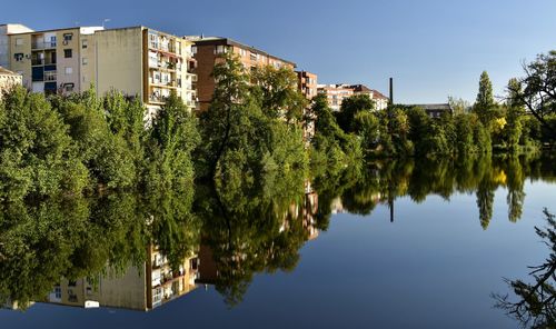 Scenic view of lake by trees and buildings against sky