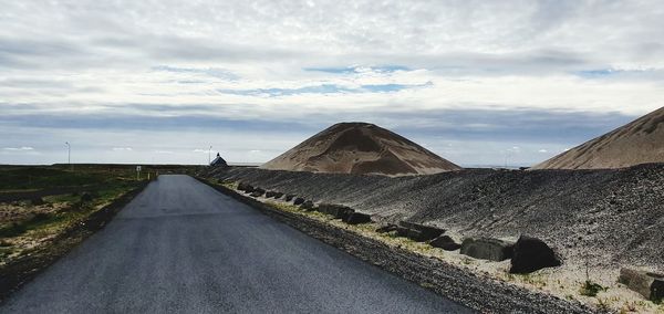 Road leading towards mountain against cloudy sky