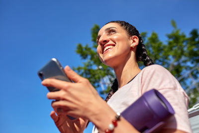 Young man using mobile phone against blue sky