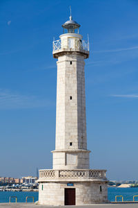 Lighthouse by sea against blue sky