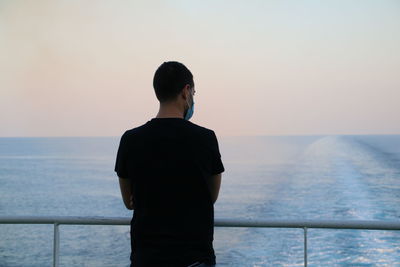 Rear view of man on a boat looking at sea against sky