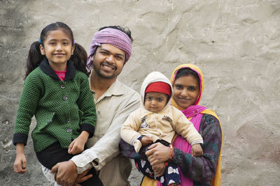 Portrait of smiling family standing against stone wall