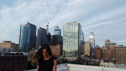 Young woman laughing against modern buildings in city