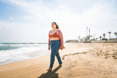 Young woman walking on beach against sky