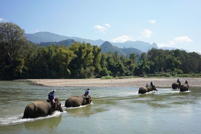 People on river by mountains against sky