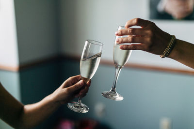 Cropped hands of friends toasting champagne flutes against wall