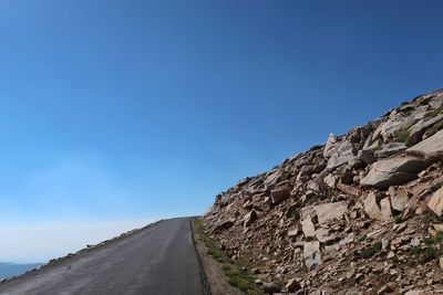 Low angle view of road amidst mountains against clear blue sky