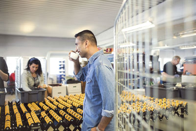 Man drinking coffee while volunteers working by production line at workshop