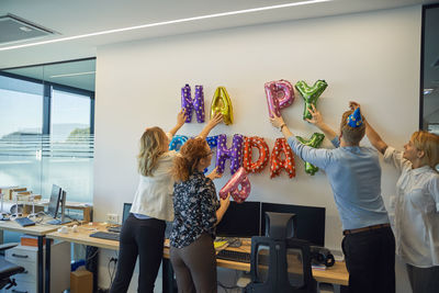 Colleagues decorating office with happy birthday writing