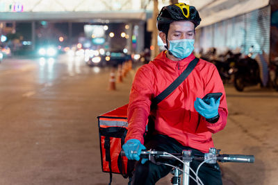 Portrait of man with bicycle standing on illuminated road