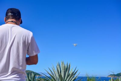 Rear view of man standing against clear blue sky