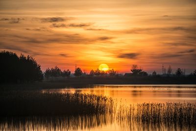 Scenic view of lake against cloudy sky during sunset