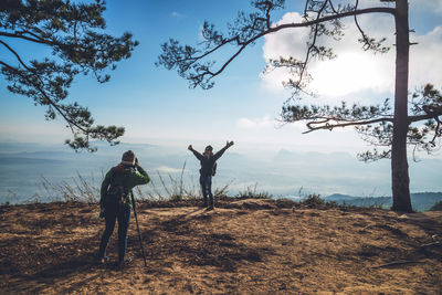 Man photographing woman with camera against sky