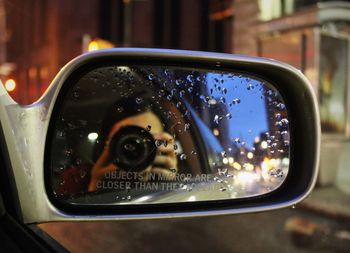 Reflection of man photographing on side-view mirror of car