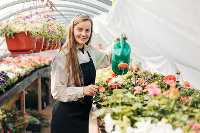 Portrait of a young gardener woman watering flowers 