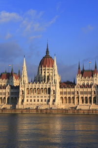 View of buildings by river against blue sky