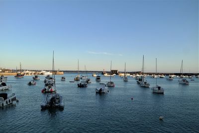 Boats in sea at harbor against clear sky