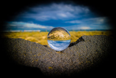 Close-up of crystal ball on beach against sky