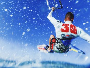 Rear view of man kiteboarding on sea against blue sky