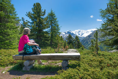 Side view of woman sitting on bench against sky